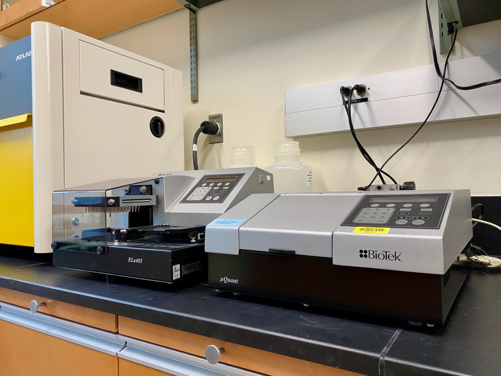 The BioTek µQuant plate reader and the ELx405 plate washer are featured, both appearing as rather small and unassuming gray box-shaped pieces of scientific equipment.