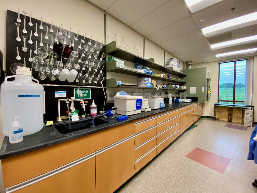 A photo of the lab bench space in ABL 313, specifically showing the fume hood on the right side of the photo. On the left side is a sink for washing glassware, with smaller scientific equipment nearby.