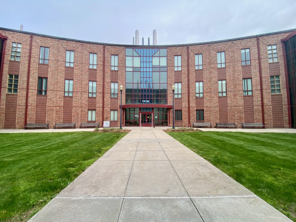 A three-floor tall semi-circle building looms in front, with a courtyard of green grass and a cement sidewalk.  This is the Agricultural Biotechnology Laboratory.